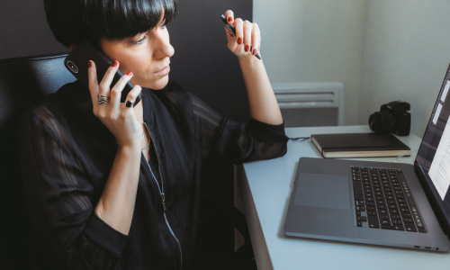 woman-sits-in-front-of-computer-talking-on-the-phone