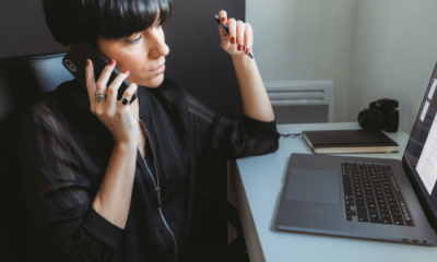 woman-sits-in-front-of-computer-talking-on-the-phone